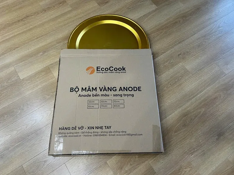 Mâm nhôm anod vàng đặt trong thùng carton in logo Ecocook và dòng chữ hàng dễ vỡ, xin nhẹ tay