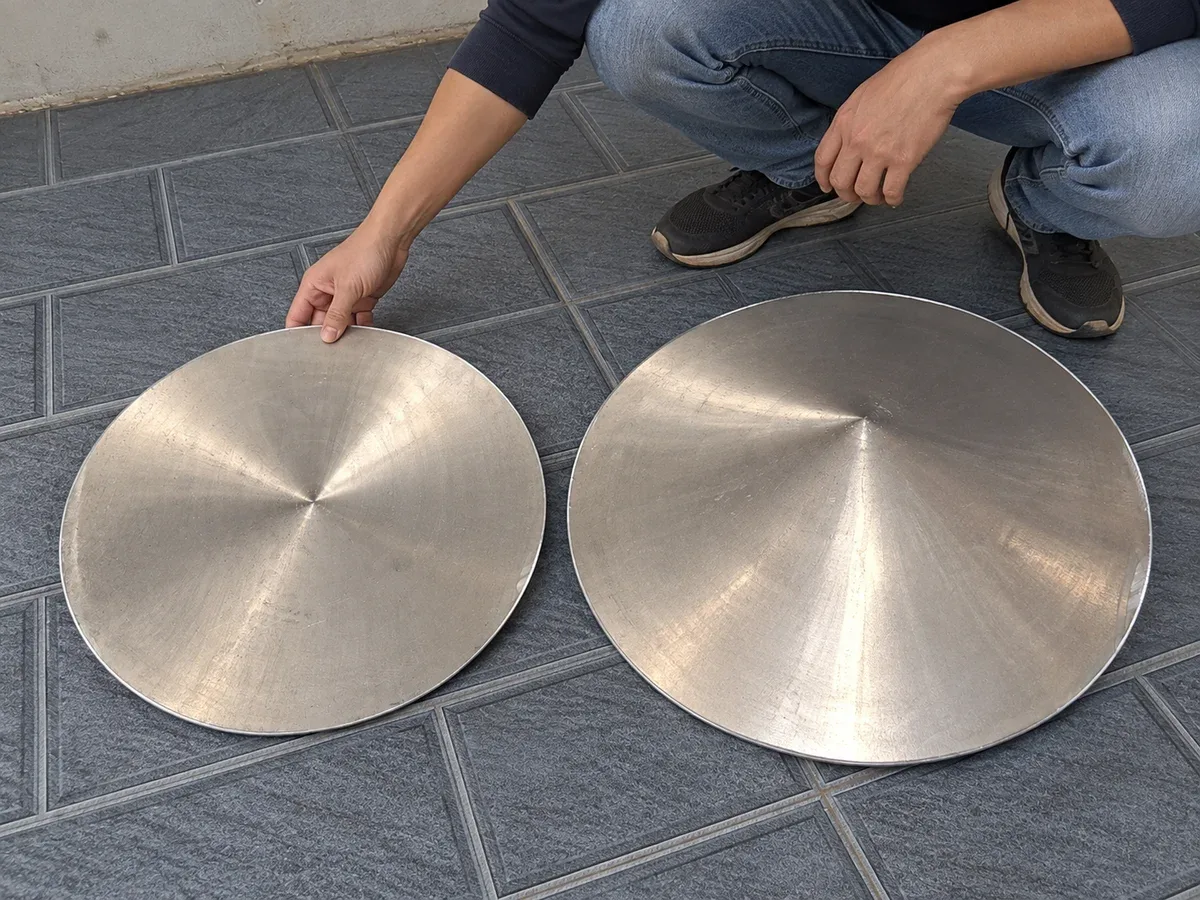 Người ngồi xổm đặt tay lên một trong hai máng nón bằng nhôm để so kích thước