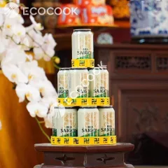 Tháp nước ngọt chữ vạn 3 tầng tròn màu vàng xếp lon bia thành hình tháp trên đôn gỗ cạnh chậu hoa lan trắng