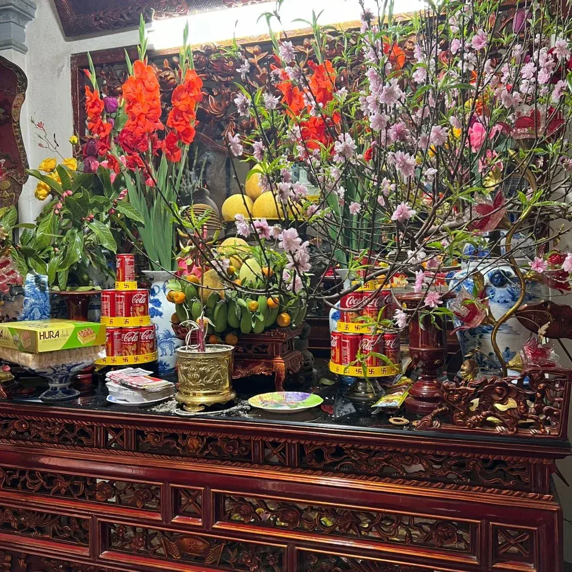 Bàn thờ gia tiên ngày Tết có hai tháp nước ngọt 3 tầng xếp lon Coca đặt hai bên, giữa là mâm ngũ quả và cành đào