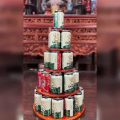 Tháp nước ngọt bằng gỗ 5 tầng tròn xếp lon bia Sài Gòn trước bàn thờ gỗ chạm