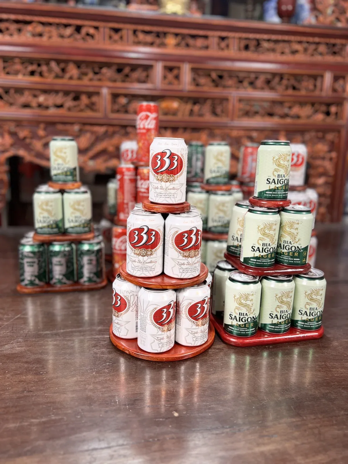 Tháp gỗ tròn xếp bia 333 và tháp gỗ vuông xếp bia Sài Gòn đặt cạnh nhau trên bàn gỗ