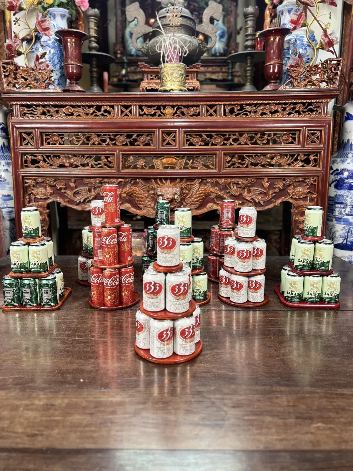 Nhiều tháp nước ngọt bằng gỗ tròn và vuông xếp lon Coca, bia 333, bia Sài Gòn bày trước bàn thờ gỗ chạm