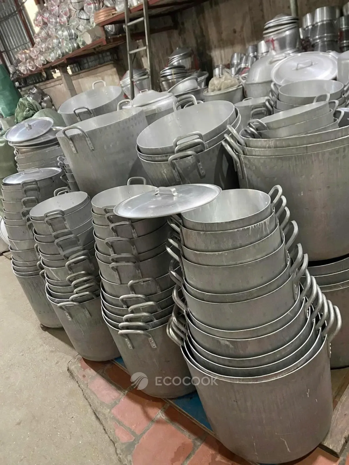 Hàng chồng nồi nhôm gò và nồi nhôm trắng nhiều cỡ xếp lồng vào nhau trên kệ trong kho xưởng Ecocook