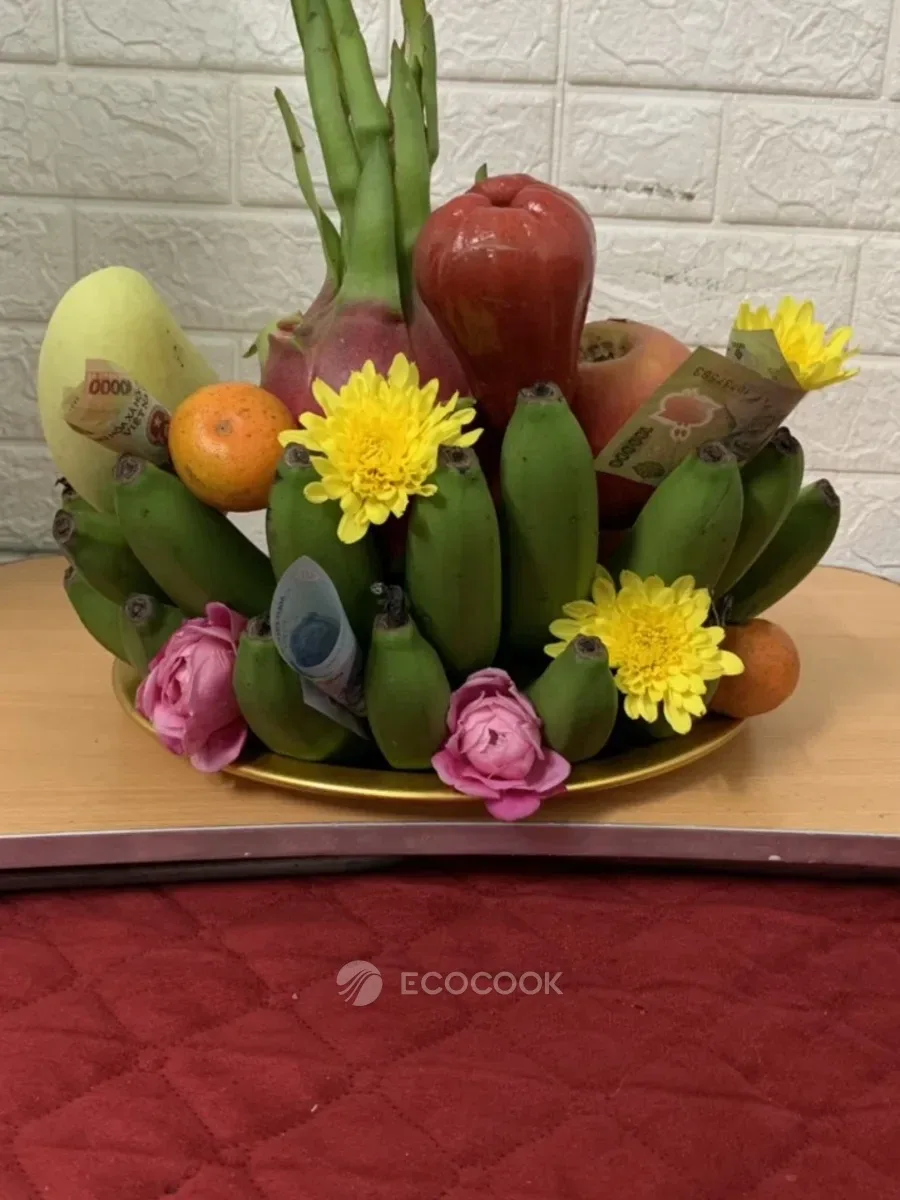 Mâm trái cây bày trên mâm nhôm vàng với chuối, bưởi, táo, cam, hoa cúc vàng và hoa sen hồng